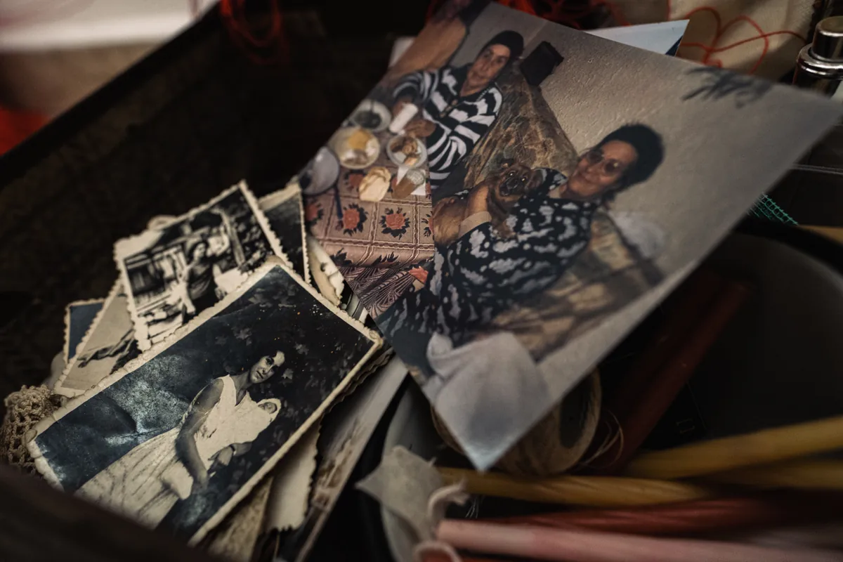 Close-up inside the open suitcase showing archival family portraits, candles, unfinished crocheted glove, and matchboxes
