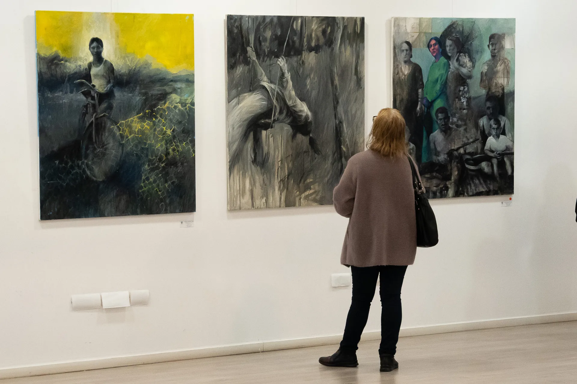 Exhibition view with visitor observing three large paintings by Andreea Gabriela Tudor