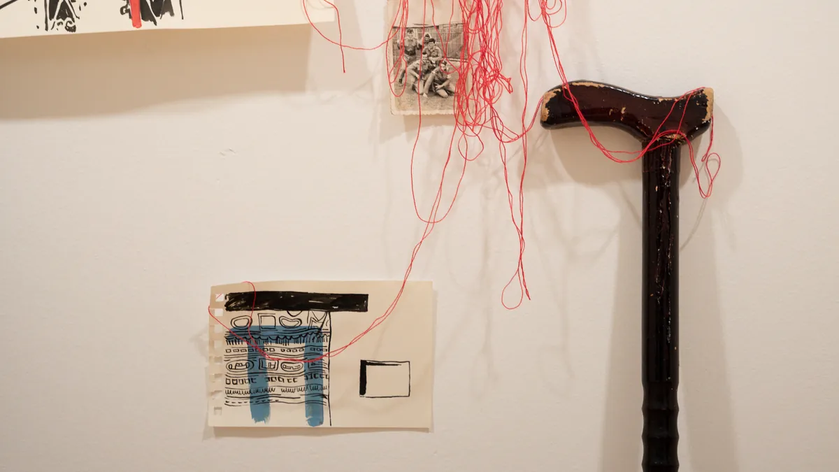 Detail of the ancestral wooden walking stick wrapped in red thread next to an archival group photo