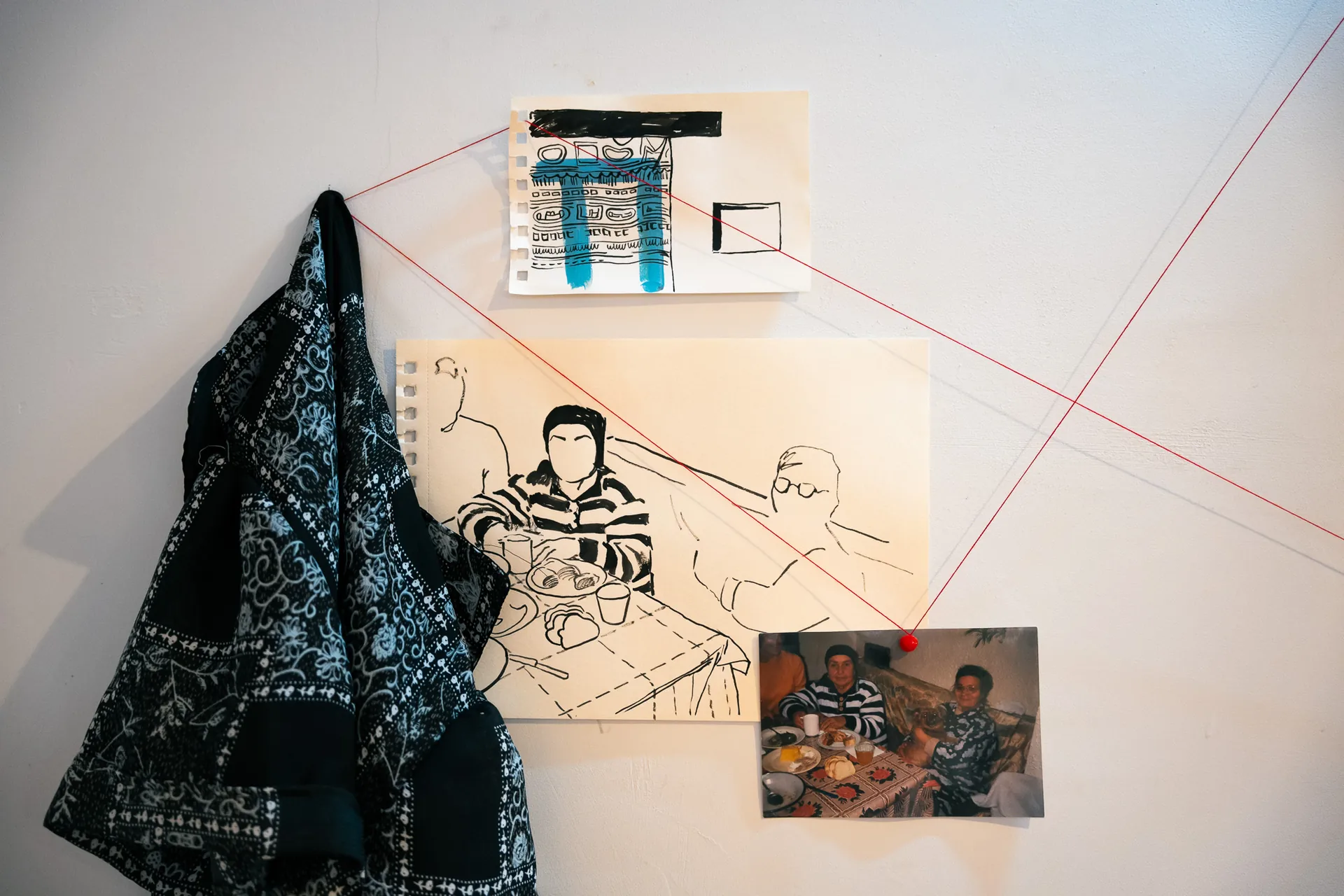 Archival family dinner photograph pinned beside its contemporary ink and acrylic drawing reinterpretation and traversed by red thread